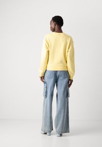 Felpa gialla con vestibilità rilassata, polsini e orlo a coste, abbinata a jeans cargo azzurri a gamba larga con tasche laterali e finitura testurizzata.
