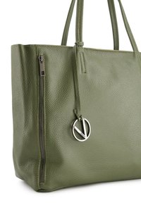 Torebka tote w oliwkowej skórze z teksturowanym wykończeniem, z bocznym zamkiem błykawicznym, regulowanym sznurkiem zamykającym oraz okrągłym metalowym logo jako akcentem.