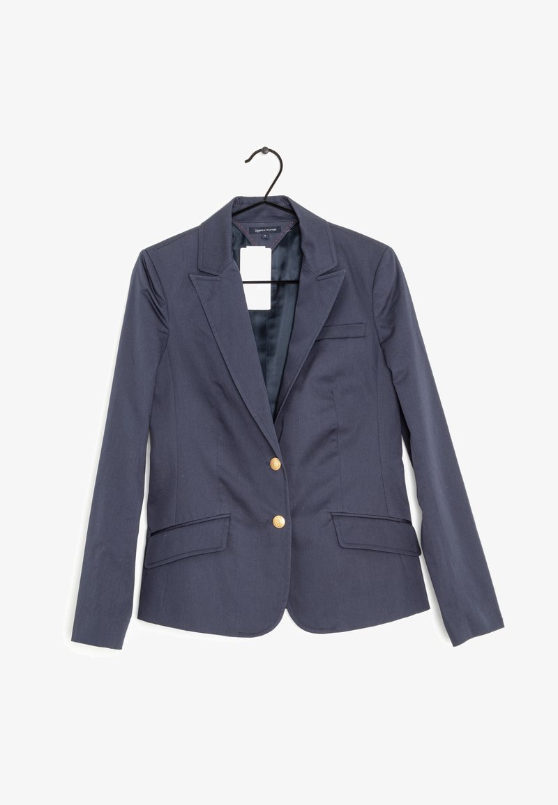 Námořnický blejzr s jednoduchým zapínáním na jeden řad, zlaté knoflíky, dvě přední kapsy a saténová podšívka viditelná v oblasti límce.