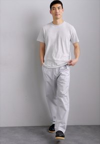 T-shirt gris, léger, à coupe décontractée, associé à un pantalon gris clair, lisse, légèrement réfléchissant et des chaussures noires sans lacets avec des semelles en bois.
