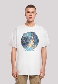 Balts kokvilnas T-krekls ar krāsainu Star Wars grafisku attēlu, kurā redzams tēls ar gaismas zobenu un teksts "STAR WARS" zils.