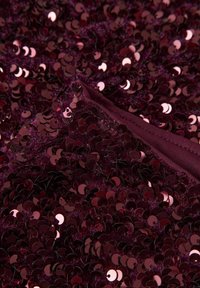 Bordo paeltega kangas, millel kattuvad ümmargused paelad, luues läikiva tekstuuri. Äärde on viimistletud pehme, ühevärvilise kangasäärisega.