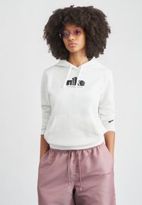 Φούτερ με κουκούλα σε ανοιχτό γκρι χρώμα με μαύρο λογότυπο, τσέπη καγκουρό και κορδόνια. Συνδυασμένο με ροζ σατέν τζόγκερ με ελαστική μέση και λεπτομέρεια λογότυπου.