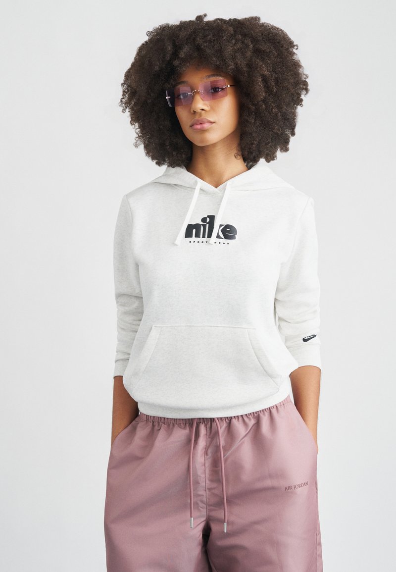 Φούτερ με κουκούλα σε ανοιχτό γκρι χρώμα με μαύρο λογότυπο, τσέπη καγκουρό και κορδόνια. Συνδυασμένο με ροζ σατέν τζόγκερ με ελαστική μέση και λεπτομέρεια λογότυπου.