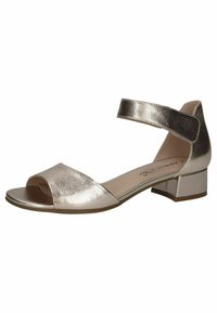 Metaliniai aukso atviri sandalai su plačia juostele priekyje ir reguliuojamu kulkšnies dirželiu. Turi žemą blokuotą kulną.