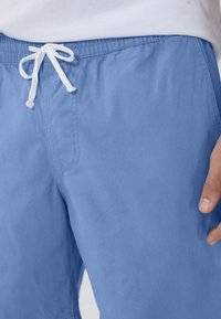 Costume da bagno azzurro chiaro realizzato in tessuto morbido, con elastico in vita e cordoncino bianco regolabile, dotato di tasca laterale.