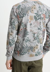 Sudadera gris con un estampado floral que presenta hojas verdes y flores multicolores. Puños y dobladillo acanalados, cuello redondo clásico.
