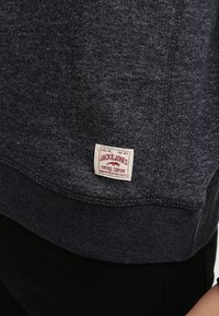 Tmavě šedá pletenina s malou bílou obdélníkovou etiketou přišnurovanou blízko lemu, na které je napsáno "Jack & Jones Vintage Company."