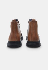 Botas de tobillo de cuero marrón con acabado texturizado, suela de goma negra y cremalleras laterales. La vista trasera muestra una forma estructurada con un detalle mínimo.