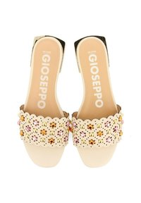 Sandalias beige de punta abierta con bordes en forma de ola, decoradas con tachuelas naranjas, rosas y doradas. Diseño plano con una textura suave y con marca destacada.