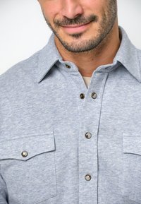 Grijze katoenen shirt met een knoopsluiting aan de voorkant, twee borstzakken met drukknoopaccenten en een klassiek kraagontwerp.