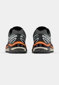 Μαύρα και γκρι αθλητικά παπούτσια με πορτοκαλί λεπτομέρεια, με υφή στο επάνω μέρος, μαξιλαράκι στη σόλα και έντονη επωνυμία στη φτέρνα.
