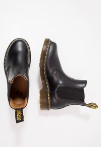 Black leather Chelsea boots with elastic sides, yellow stitching, and a brown rubber sole, featuring a pull tab for easy wear.