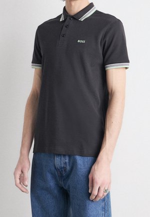 Polo gris foncé avec un col et des poignets à rayures contrastantes vertes et blanches, présentant un petit logo brodé sur la poitrine.