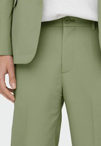 Pantalones de traje verde claro hechos de una tela suave, con frente plano, presillas para cinturón y cierre de un solo botón.
