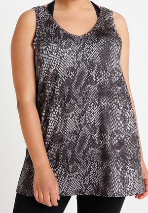 Kobieta nosząca czarny i szary bezrękawnik w wężowy wzór na czarnym sportowym staniku, w połączeniu z czarnymi legginsami.