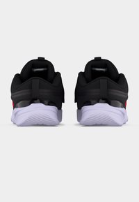 Ζευγάρι μαύρα και λευκά αθλητικά παπούτσια με παχιά λευκή σόλα, φαίνονται από πίσω σε λευκό φόντο.