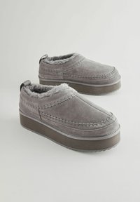 Grå ruskinds slip-on sko med et blødt pelsfor, tyk platformssål og kontrasterende syninger. Designet til komfort og nem påføring.