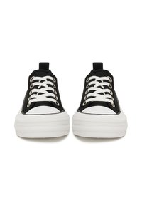 Zapatillas deportivas de lona negra con suela de goma blanca, con punta redonda, cordones blancos y ojales de metal. Diseño delgado con lengüetas de tela para tirar.
