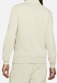 Ljusbeige sweatshirt med hög krage, ribbad mudd och nederkant. Slät textur med sidfickor och minimala sömnadsdetaljer.