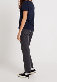 Marinblå t-shirt med kort ärm, kombinerad med grå raka jeans och svarta sneakers med vita detaljer, sedd från sidan.