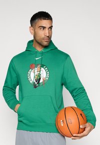 Πράσινο φούτερ με κουκούλα και μεγάλο λογότυπο των Boston Celtics που απεικονίζει έναν λεπτριχάνο που κρατάει μια μπάλα μπάσκετ. Μπροστινή τσέπη τύπου καγκουρό, κουκούλα με κορδόνια και απαλή υφή.