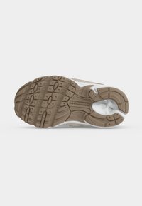 Πάτος ενός sneaker New Balance που δείχνει πατενταρισμένη καφέ λαστιχένια εξωτερική σόλα και λευκή ενδιάμεση σόλα με το λογότυπο New Balance στο κέντρο.
