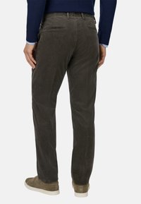 Donkergroene corduroy broek met rechte pijpen, tekstuurstof, twee achterzakken en gedragen met beige suède sneakers.