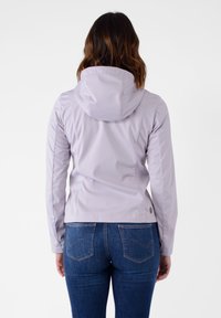 Giacca impermeabile di un viola chiaro con design aderente, cappuccio attaccato e polsini elasticizzati, abbinata a jeans blu scuro con cuciture sulle tasche.