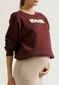 Bordeaux sweatshirt met geborduurde "mom" tekst, met lange mouwen en een relaxte pasvorm, gecombineerd met beige geribbelde leggings.