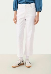 Vita, korta jeans med avslappnad passform och hög midja, med knappstängning och subtila stickningsdetaljer, kombinerat med beiga sneakers.