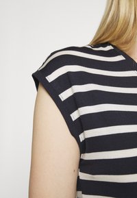 Camisa listrada em azul-marinho e creme, com mangas curtas e um tecido macio e texturizado. Costuras visíveis nos ombros.