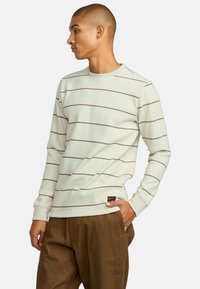 Crème kleurige longsleeve shirt met bruine horizontale strepen, geribbelde structuur en een ronde halslijn. Etiket bevestigd aan de zoom.