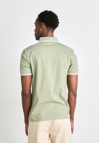 Polo en vert clair, manches courtes, col et poignets en côtelé blanc, fabriqué en coton, texture lisse, vue de dos affichée.