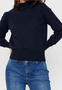 Marine blauw gebreid sweater met een hoge nek, voorzien van een gewatteerd patroon en ribgebreide zoom. Gecombineerd met blauwe high-waisted jeans.