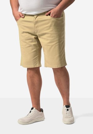 Shorts beiges en coton à coupe droite, dotés de poches avant, associés à des baskets blanches avec des accents noirs et des lacets.