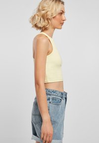Vaaleankeltainen istuva crop-top, jossa on olkaimet, yhdistettynä korkean vyötärön vaaleansinisiin farkkushortseihin, joissa on käänteet ja erottuva ommel.