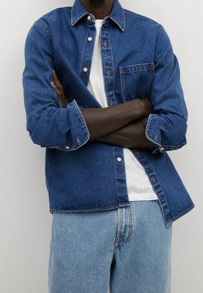 Denim overhemd in medium blauw met een knoopsluiting aan de voorkant, klassieke kraag, enkele borstzak en lange mouwen opgerold bij de manchetten. Draag het over een wit T-shirt.