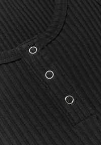 Maglione nero a coste con scollatura arrotondata e tre chiusure a cerchio metalliche nella parte anteriore. Texture morbida con righe verticali.