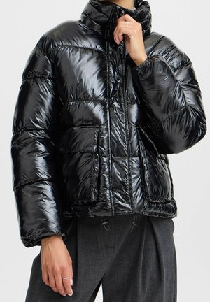 Doudoune noire avec un extérieur brillant et matelassé, col montant, fermeture éclair et poches avant. Présente un ourlet et des poignets élastiques.
