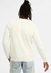 Lichtbeige trui met lange mouwen, zachte textuur, geribde manchetten en zoom, en een minimalistisch ontwerp. Gegaans met lichtblauwe denimspijkerbroek.