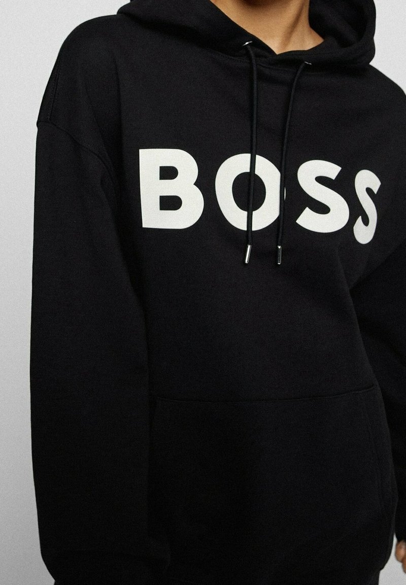 Schwarzer Kapuzenpullover aus weichem Material mit einem großen weißen "BOSS"-Logo auf der Vorderseite, Kordelzug-Kapuze und vordertasche.