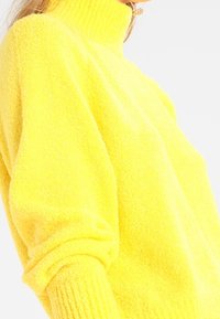 Bright yellow, high-neck pullover sweater made of soft, textured fabric; features ribbed cuffs and relaxed fit.