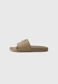 Brune glidelsesandal med en teksturert stropp, som har en hevet logo. Laget av formet gummi, har den en flat såle og minimalistisk design.