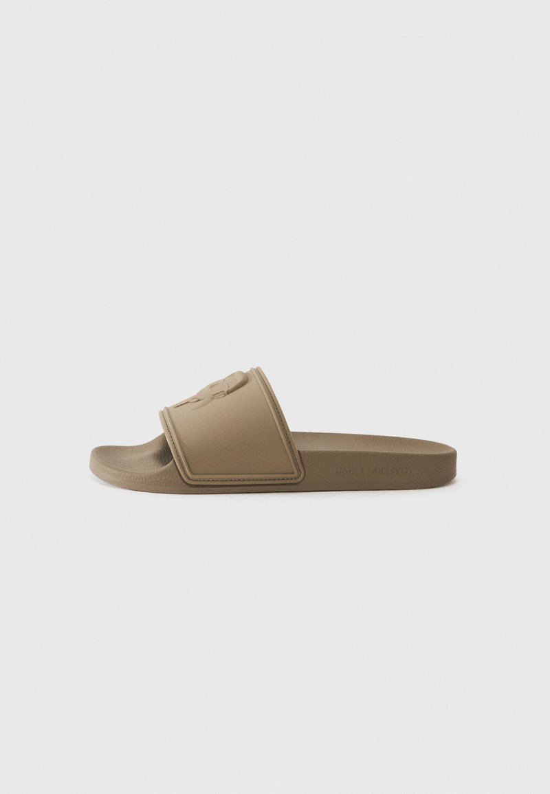 Brune glidelsesandal med en teksturert stropp, som har en hevet logo. Laget av formet gummi, har den en flat såle og minimalistisk design.