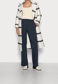 Takki mustavalkoruudullisella kuviolla, kerma valkoinen toppi, tummansininen leveälahkeiset housut ja vaaleat korolliset saappaat.