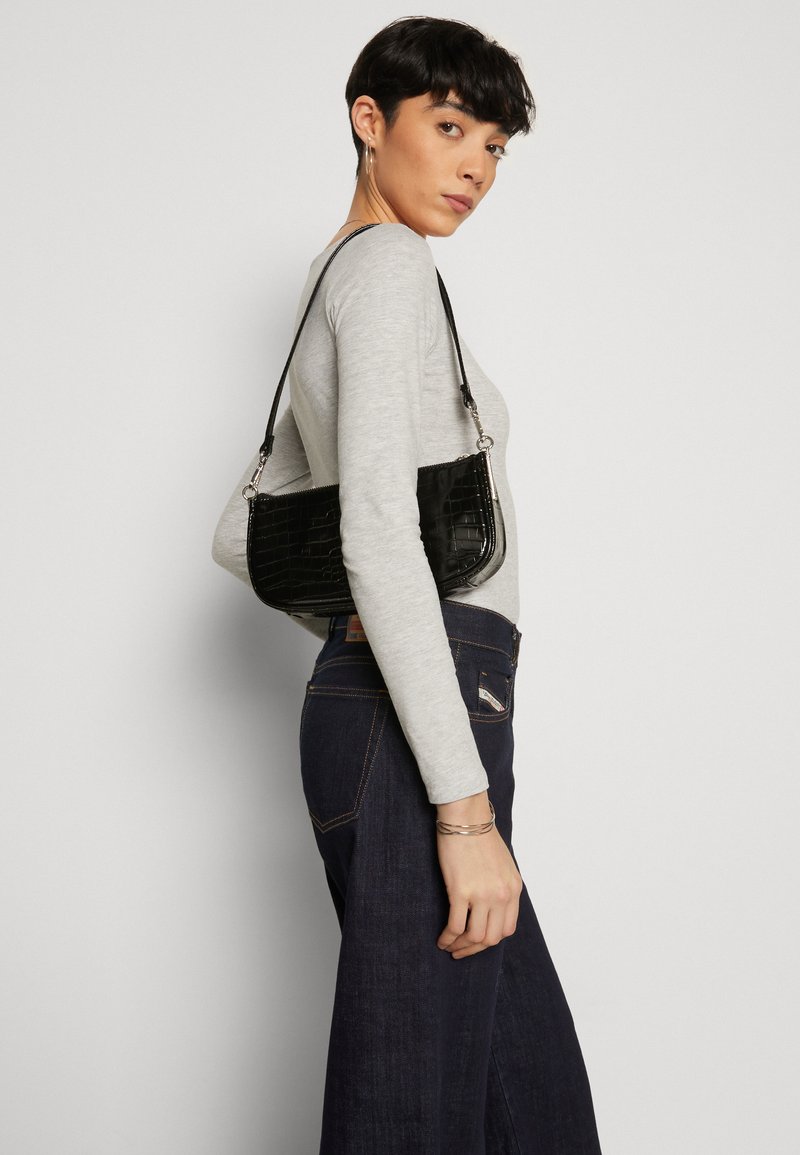 Bolso de mano de imitación de cocodrilo negro con una correa delgada, forma rectangular, textura suave y herrajes en plata, llevado al hombro.