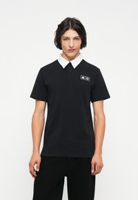 Polo negru din bumbac, cu guler alb, mâneci scurte și o mică etichetă cu logo pe pieptul stâng. Design simplu și clasic.