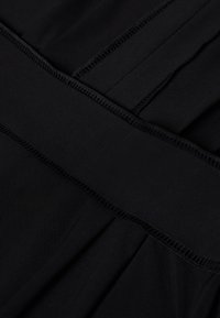 Musta kangas, sileä pinta, leveällä joustavalla vyötärönauhalla ja huolellisesti ommelluilla reunoilla. Suunnittelussa on tarjottu laskoksia ja minimaalista yksityiskohtaisuutta.