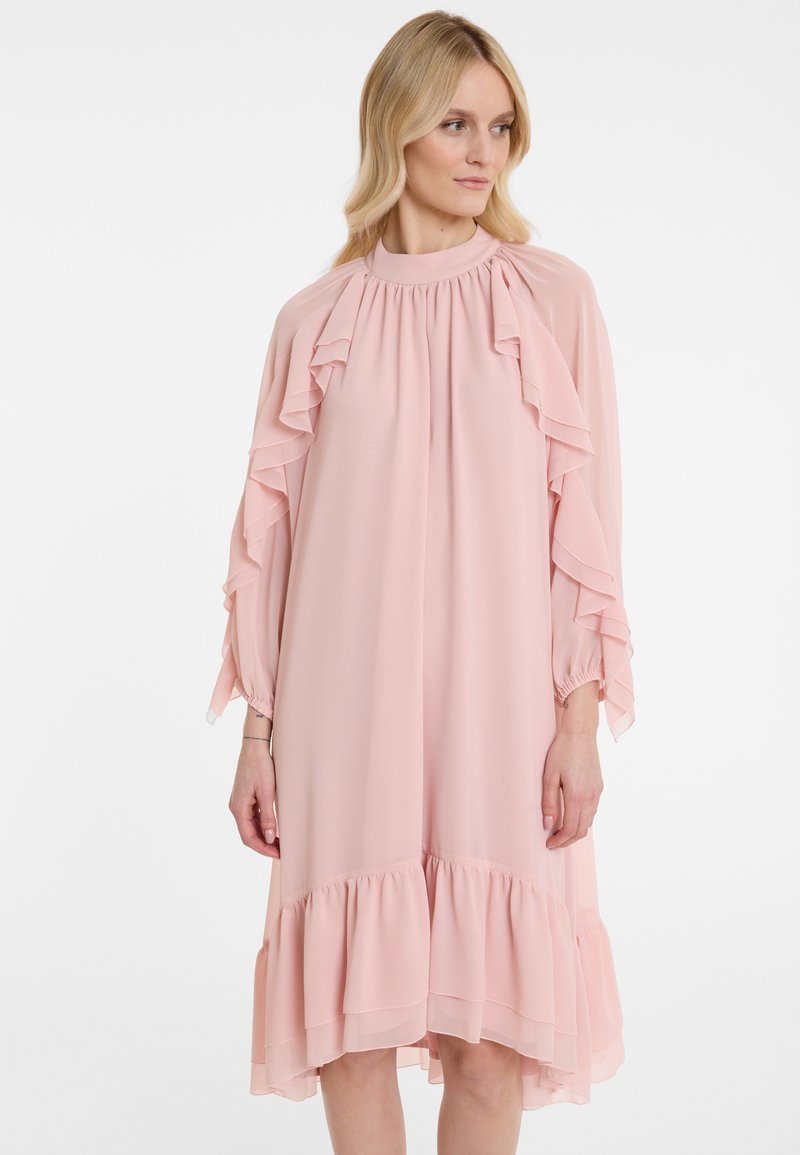 Helles rosa Kleid aus fließendem Stoff, mit Rüschendetails an den Ärmeln und dem Saum, in lockerer Passform und mit hohem Kragen.